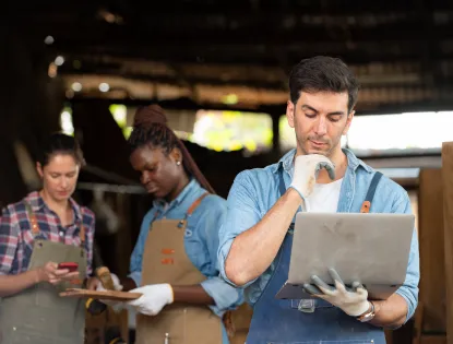 a man working hard in an apron holding and looking at a laptop