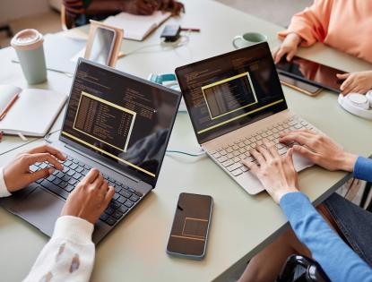 Close up photo of two women's hands coding on two laptops