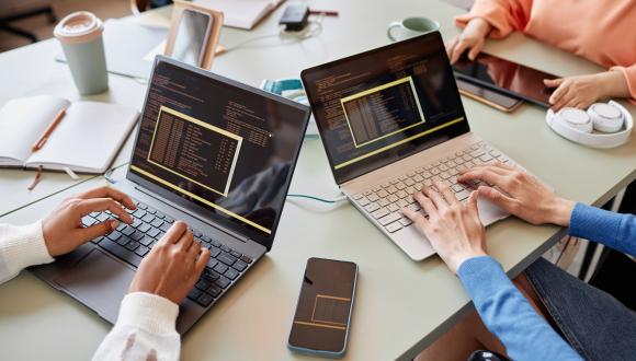 Close up photo of two women's hands coding on two laptops