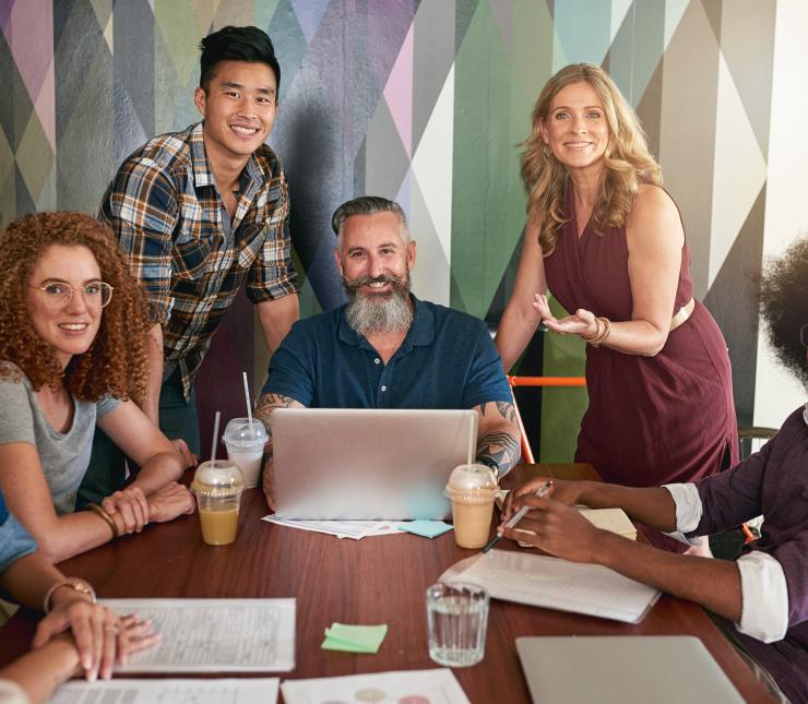 a group of smiling men and women gathered at a table around a laptop